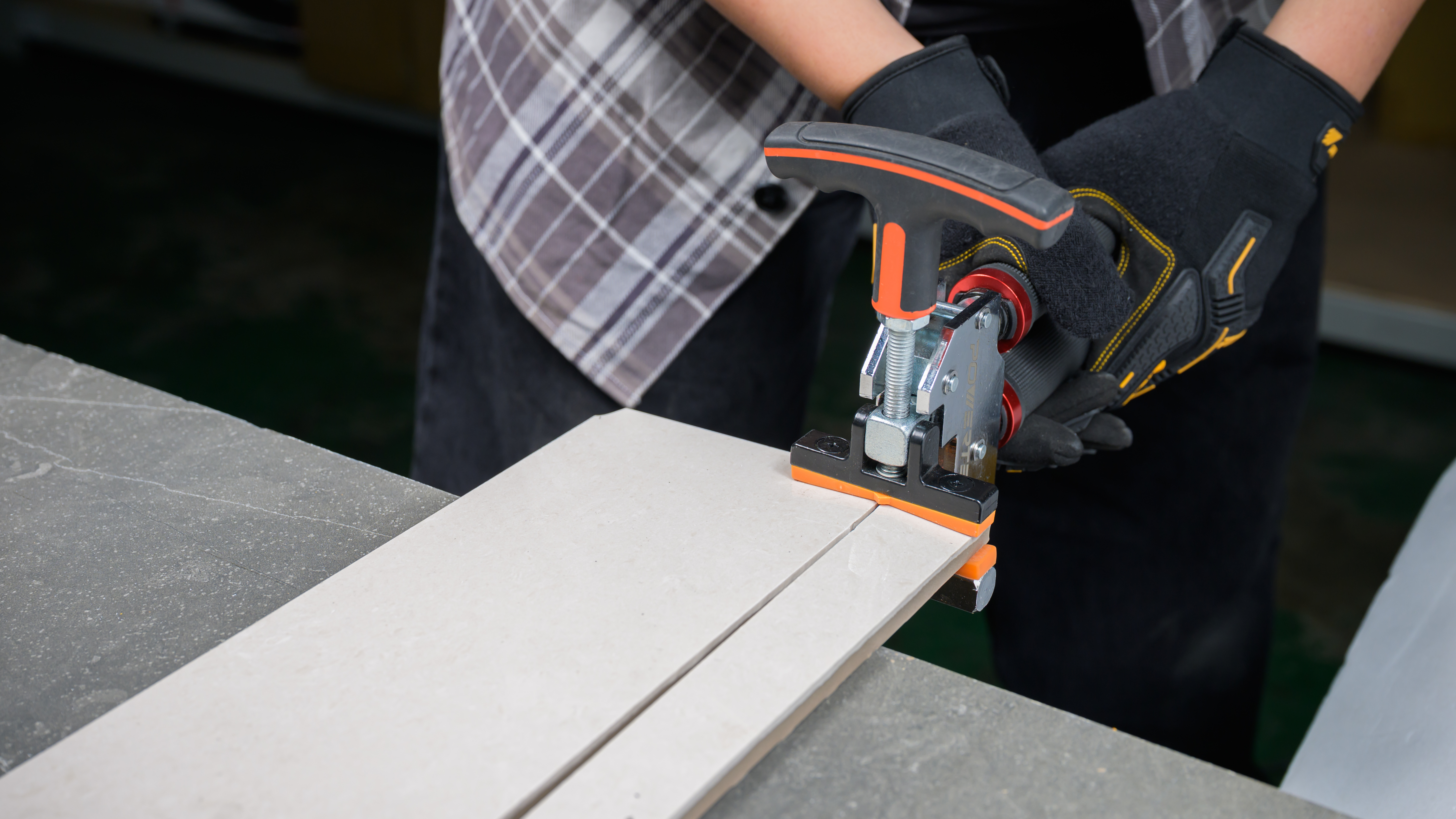 DIYer scoring and snapping a large-format porcelain tile using Powertec manual cutter and breaker tool